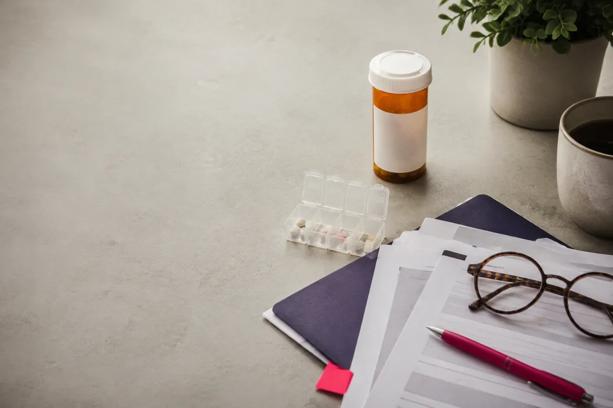 Prescription medication bottles, a weekly pill organizer, and Medicare planning materials arranged on a desk.