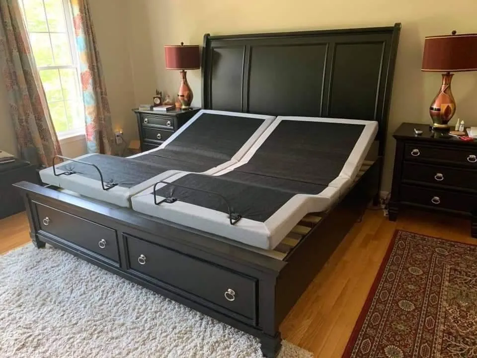 an image of a split king adjustable base with the head and feet raised slightly. no mattress on it. the base is inside a nice dark colored bed frame.