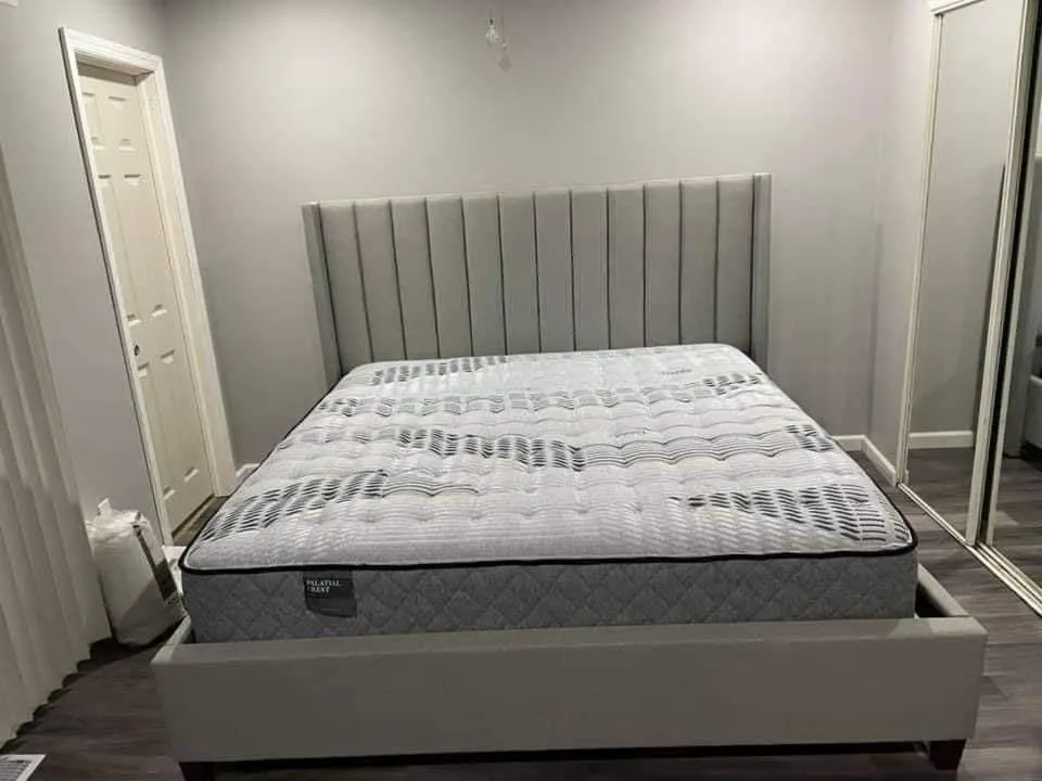 A plush mattress with a grey border and a white top. The white top has blue stripes on it. Made by Sealy