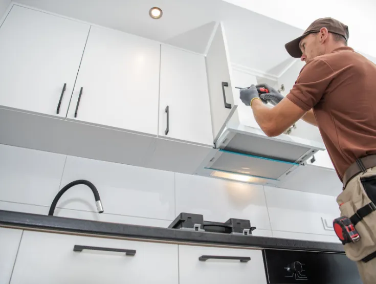 Professional handyman repairing kitchen cabinet in modern white kitchen providing expert home repair and maintenance services for homeowners in North Carolina