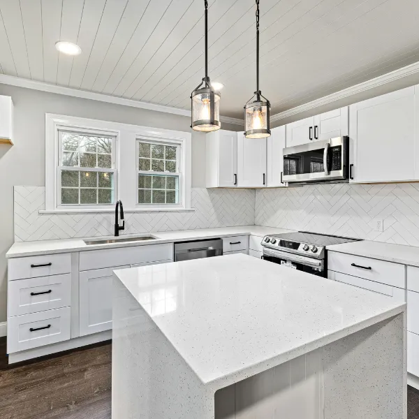 Modern white kitchen renovation with quartz island pendant lighting and stainless steel appliances installed by professional remodeling contractors in North Carolina