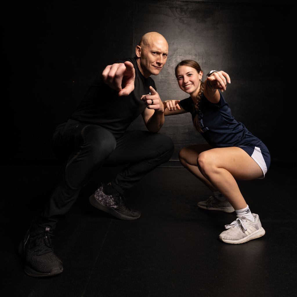 Coach Justin Kegley and a female athlete pointing at the camera in a squat stance