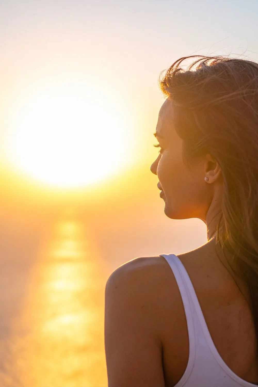 Calm woman seated in natural light, hands resting on knees, symbolizing nervous-system regulation and somatic healing.