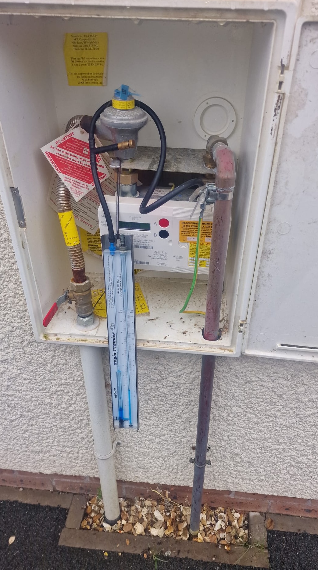 Gas Safe engineer using a U-gauge manometer to perform a domestic gas tightness test at a meter box in Plymouth