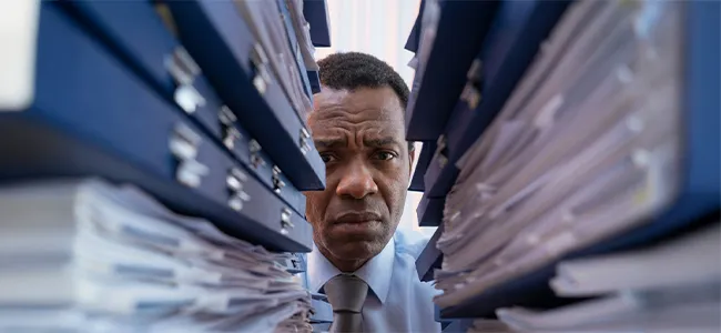 An image of a man staring through 2 large stacks of files
