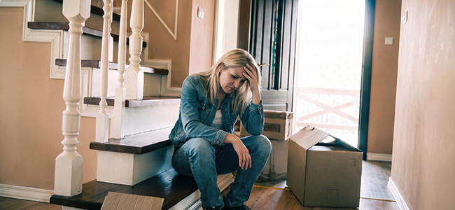 A woman sitting on her steps with boxes around her sad that she has to leave her home