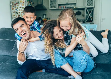 Parent with kids on their backs while sitting on a couch. Everyone is smiling and laughing. | Te Busy Parent's Guide to Improving Connection in 20 Minute Per Day