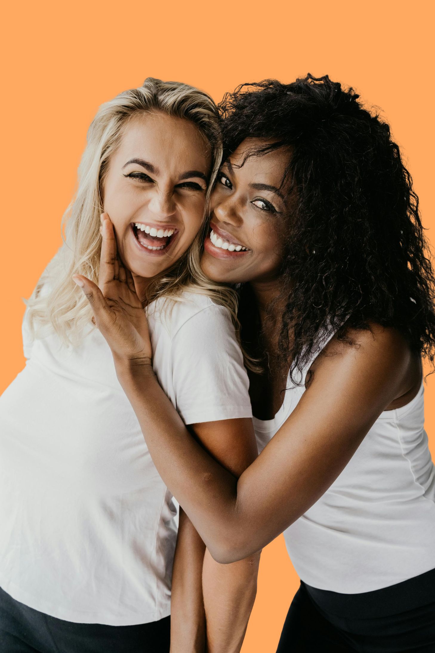 2 women smiling in front of an orange background