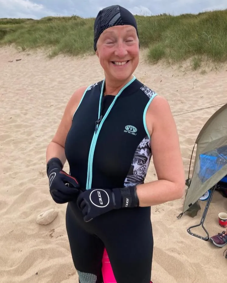 The same woman smiling on the beach in her wetsuit