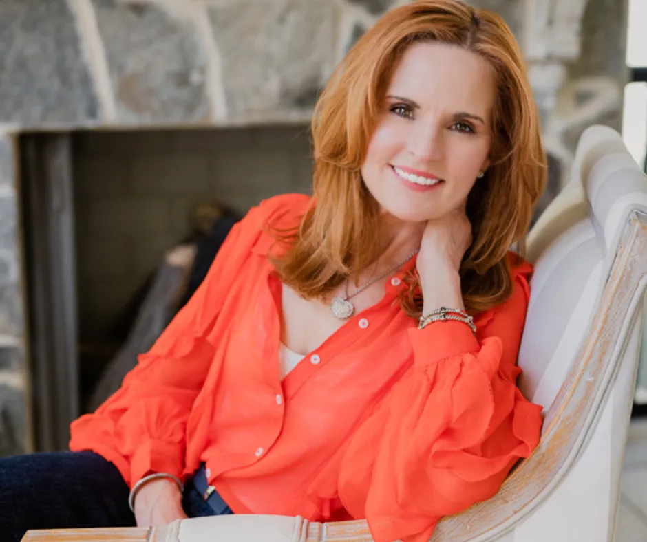 Annie Bauer, Founder of The Sovereign Mind in an orangle blouse seated in front of a fireplace