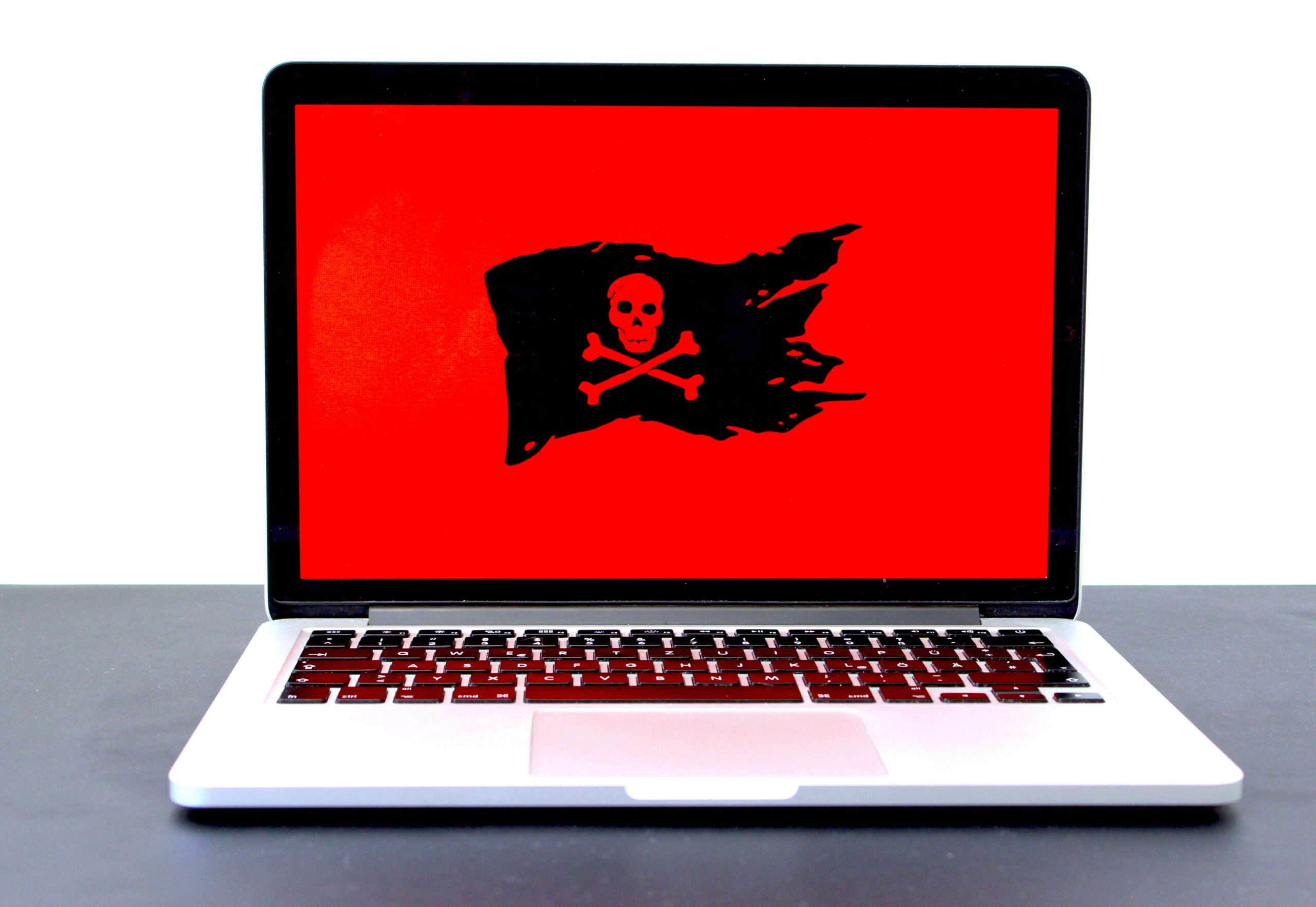 A laptop showing a red screen with a black pirate flag on it. 