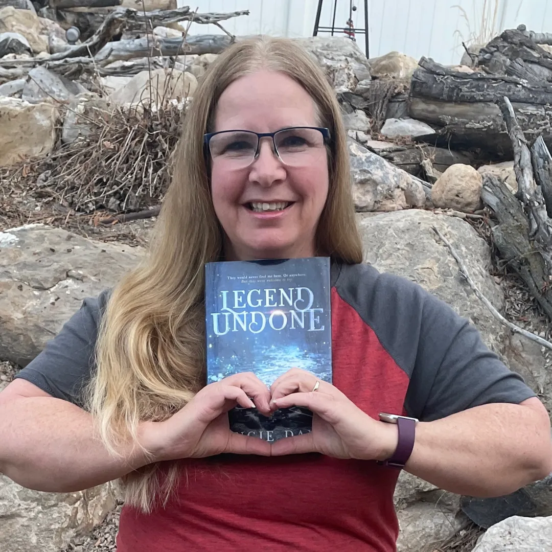 Reader making heart shape while holding Legend Undone clean romantasy book