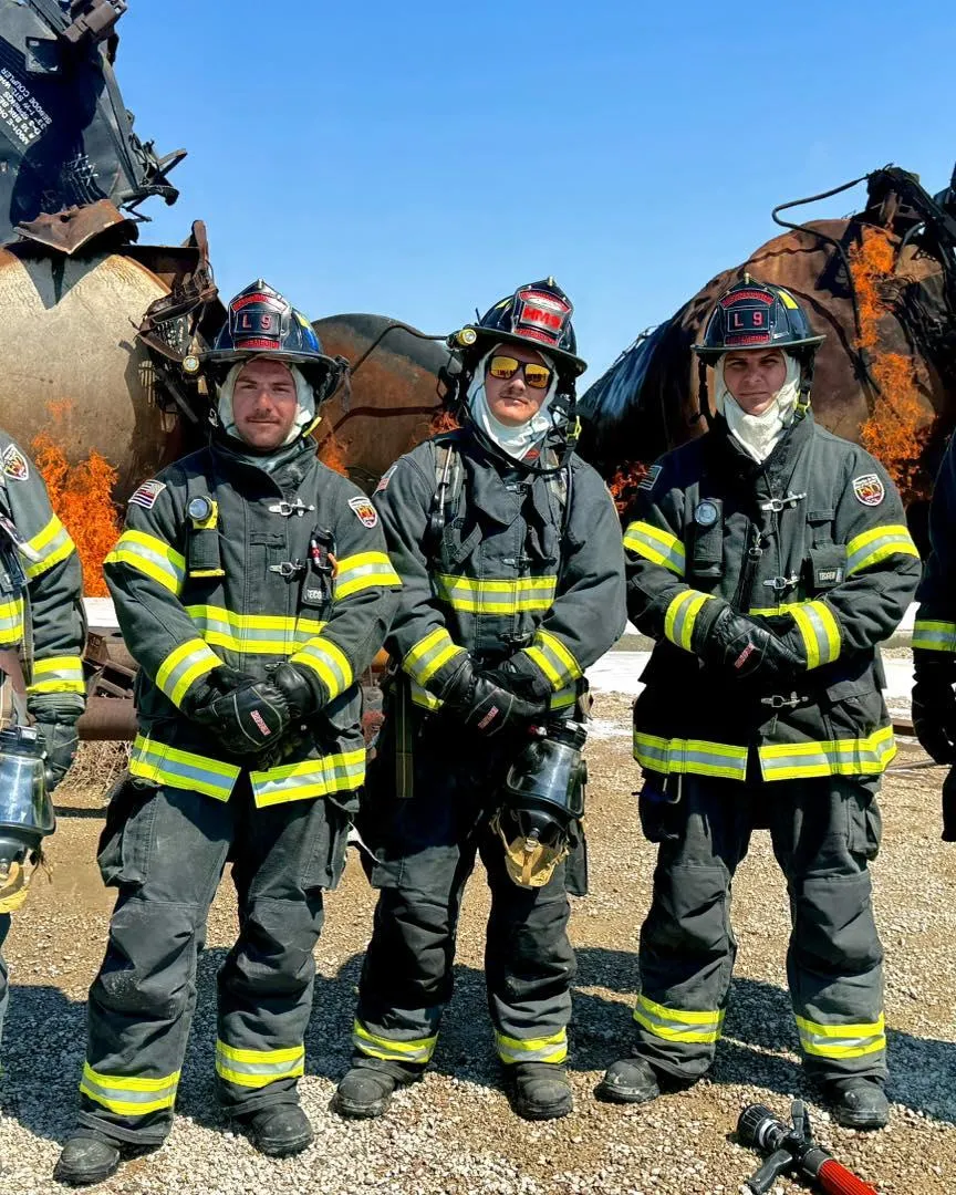 Pasco County Professional Firefighters in full turnout gear standing in front of a live fire training simulation with burning wreckage