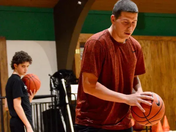 Basketball player practicing dribbling with coach supervision.