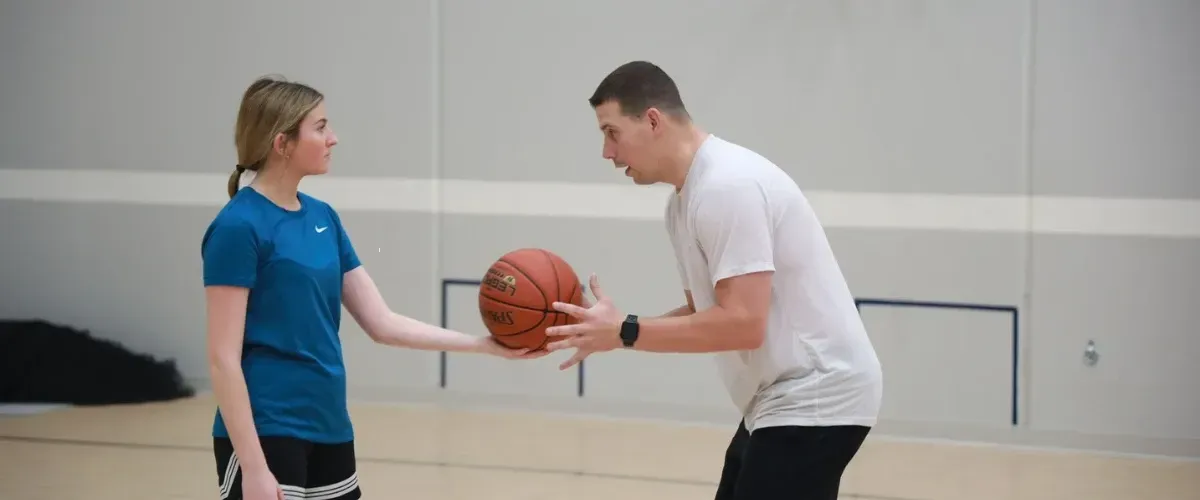 Basketball coach guiding a young player during a one-on-one training session in the gym.