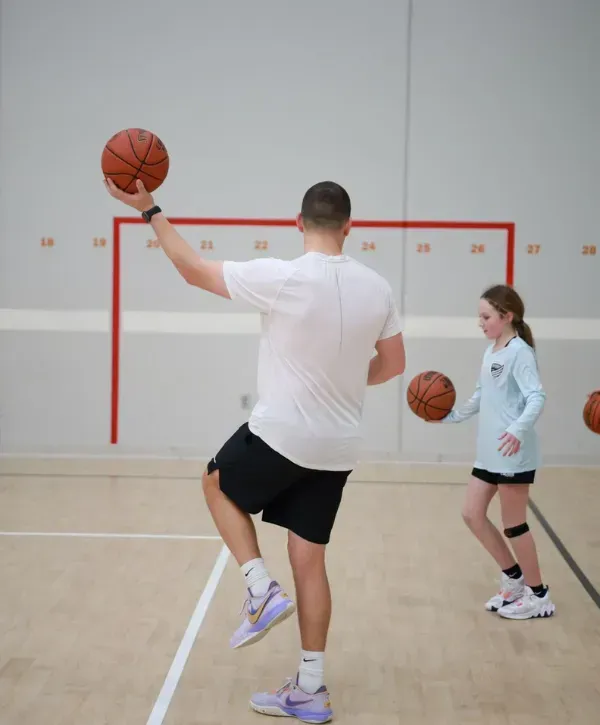 Basketball coach demonstrating a drill to a young player during practice in a gym.