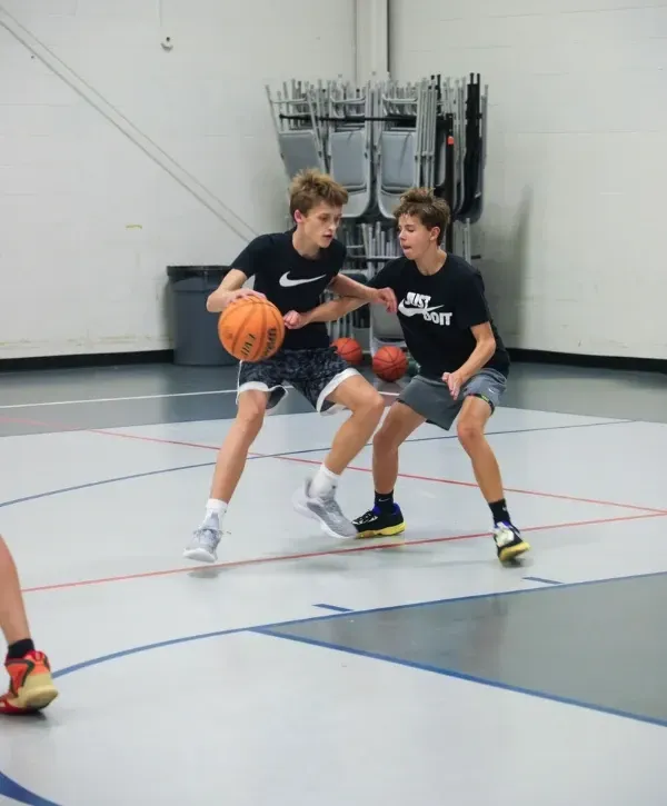 Teen players practicing one-on-one basketball defense and ball handling in a gym.