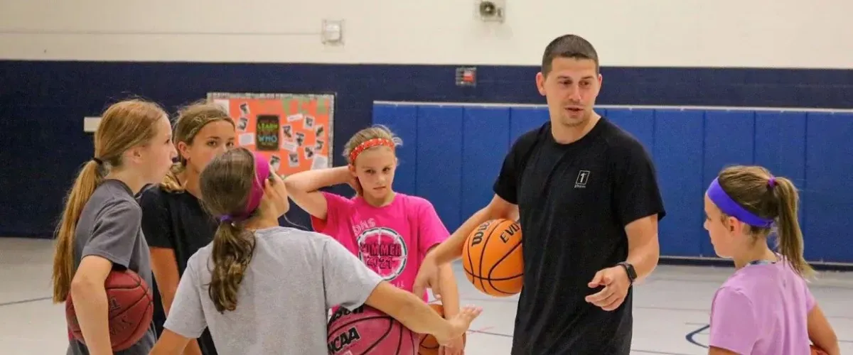 Coach teaching basketball fundamentals to girls during a youth training session.