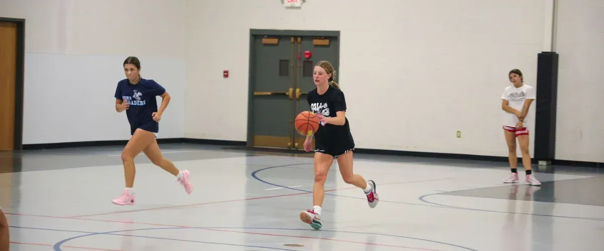 Girls practicing basketball dribbling during indoor training session.