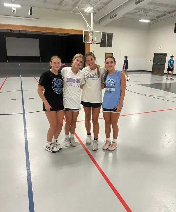 Group of teenage girls posing on indoor basketball court.