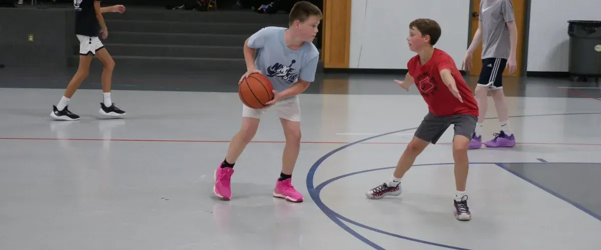 Youth player practicing a layup drill with a coach assisting during basketball practice.