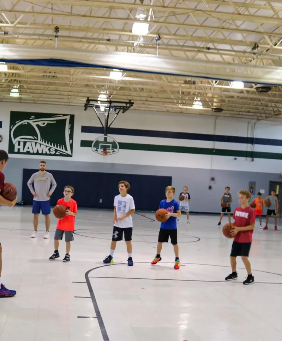 A group of young men training with basketballs in a gymnasium, led by a man dribbling in the foreground.