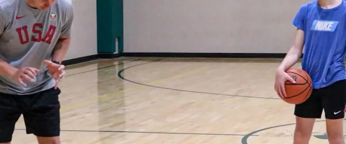 Two boys compete for a basketball on a gym court, one in goggles holding the ball, the other defending.