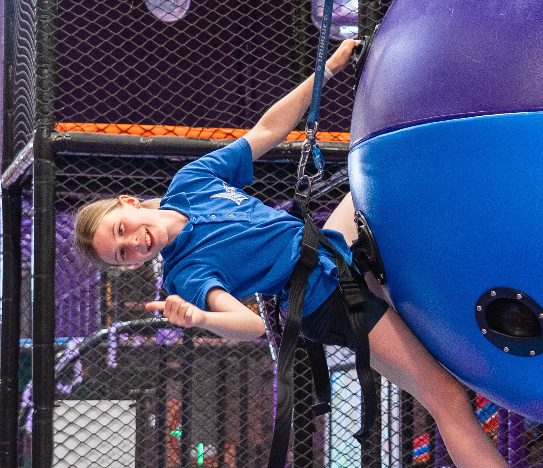 A large school assembly in a bright gymnasium, with students and teachers enthusiastically participating in a group wellness activity. The atmosphere is energetic and supportive, with banners and colorful mats adding vibrancy to the scene.
