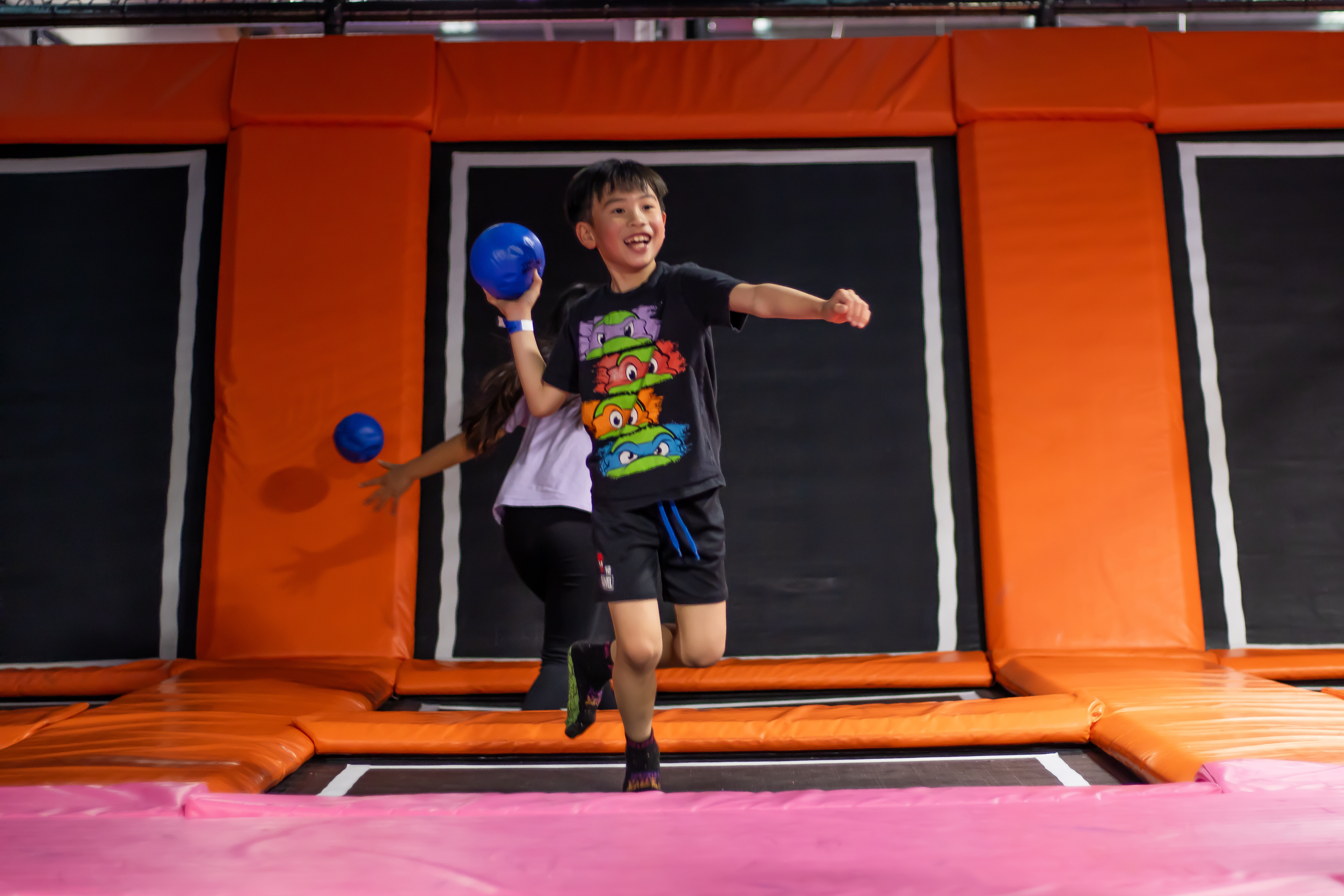 A large school assembly in a bright gymnasium, with students and teachers enthusiastically participating in a group wellness activity. The atmosphere is energetic and supportive, with banners and colorful mats adding vibrancy to the scene.
