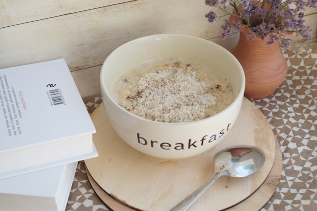 A bowl of oatmeal with cinnamon beside an open book and dried lavender on a warm wooden surface, representing simple, nourishing eating for people managing MS symptoms.