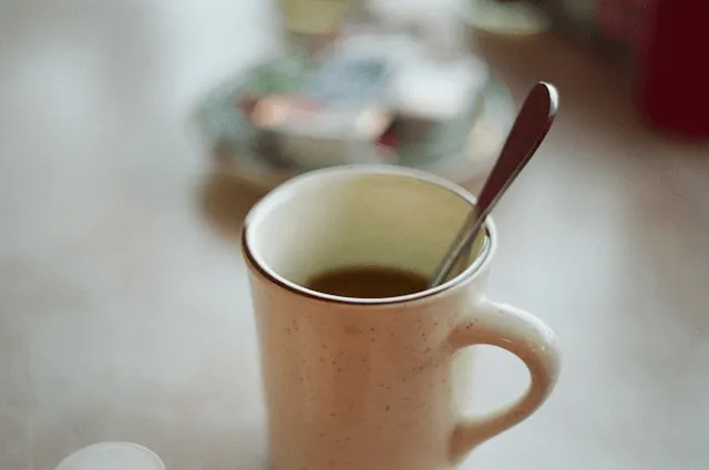 A close-up of a speckled mug with a spoon in it, filled with coffee..