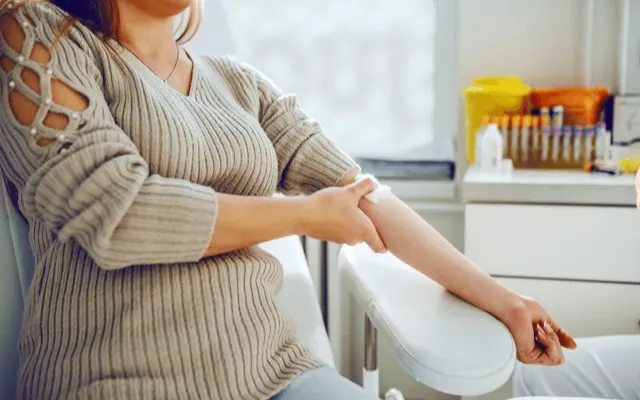 A woman seated in a clinic with her sleeve pushed up and arm resting on the chair, waiting for a blood draw to check for nutrient deficiencies.