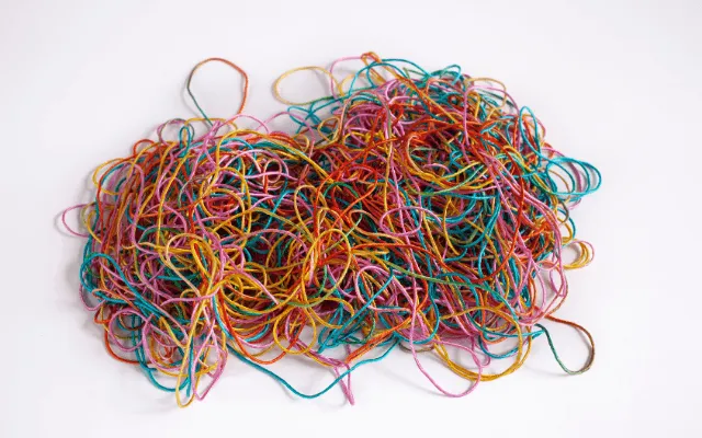 Tangle of multicolored threads on a white background — a visual metaphor for how sleep, movement, stress, and mental health intertwine with MS fatigue..