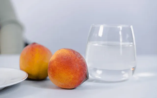 Two whole peaches beside a glass of water — a small, cool snack for appetite loss during summer heat with MS.