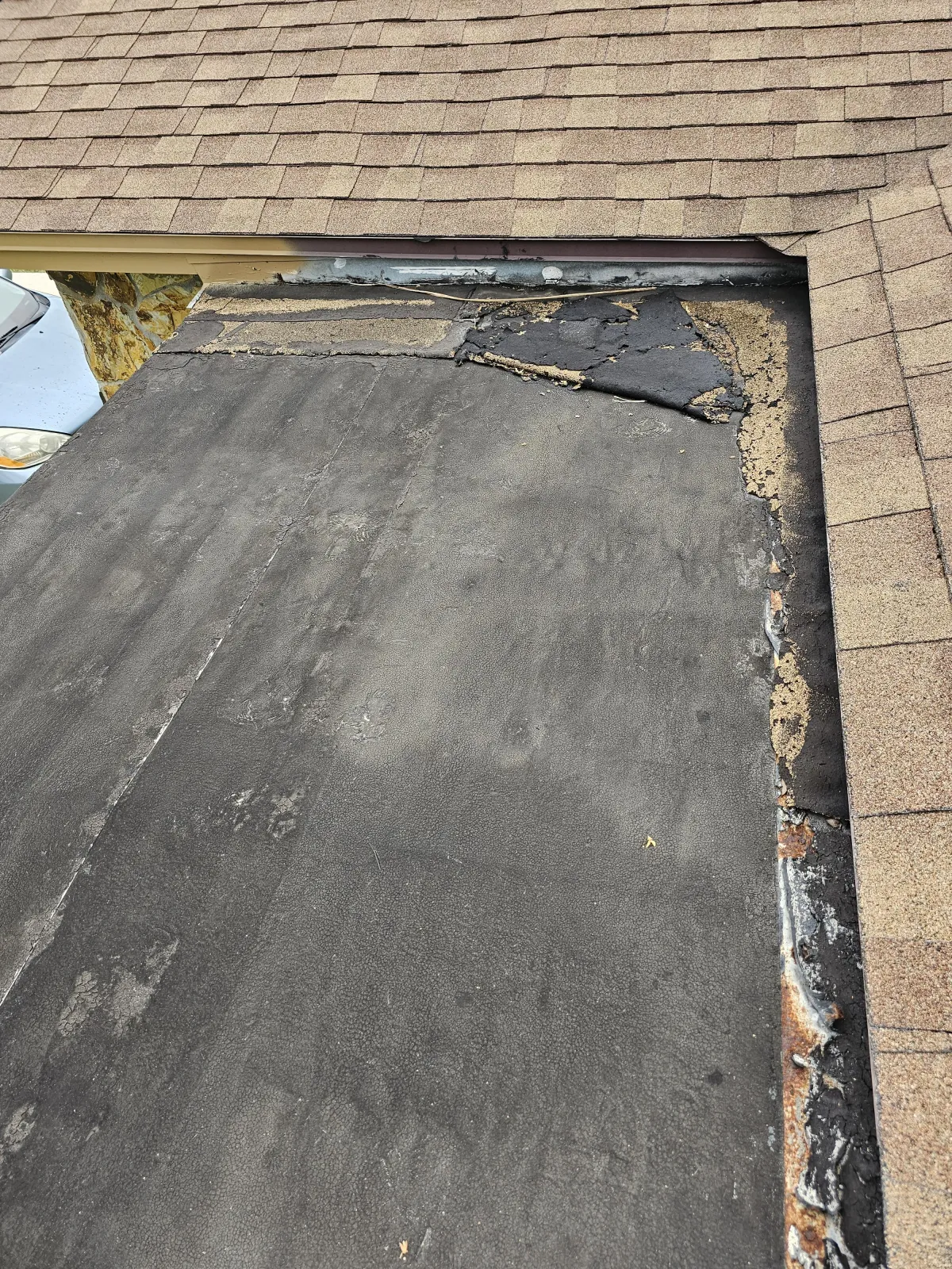 Close-up of torn shingles and ridge cap at a leak point before replacement.