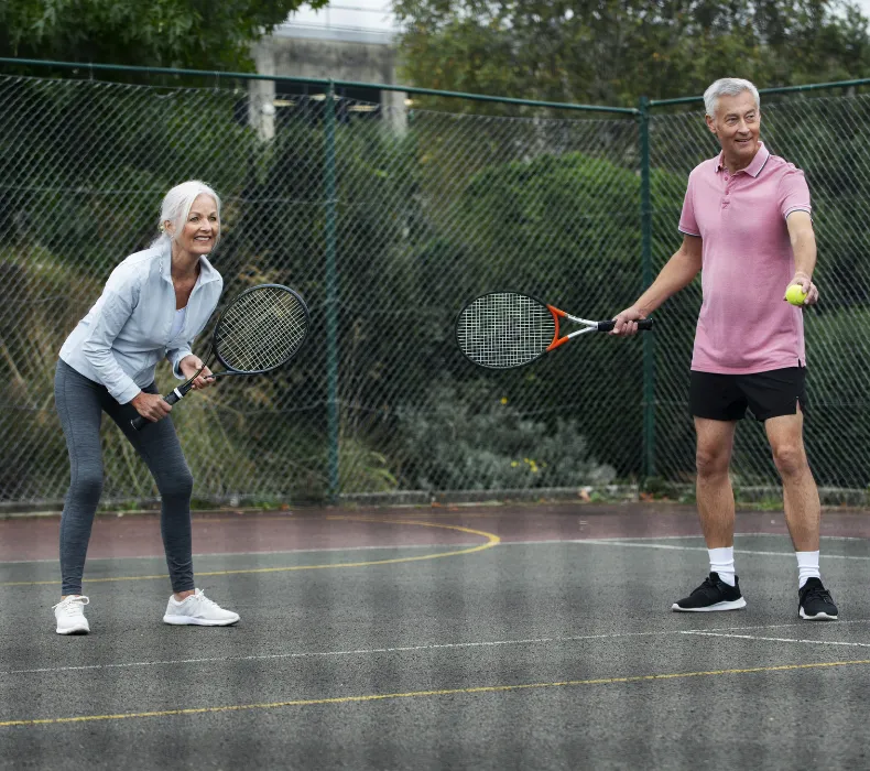 Active older couple playing tennis outdoors, smiling and pain-free, representing restored mobility and improved quality of life after pain relief treatments in Cupertino, CA.
