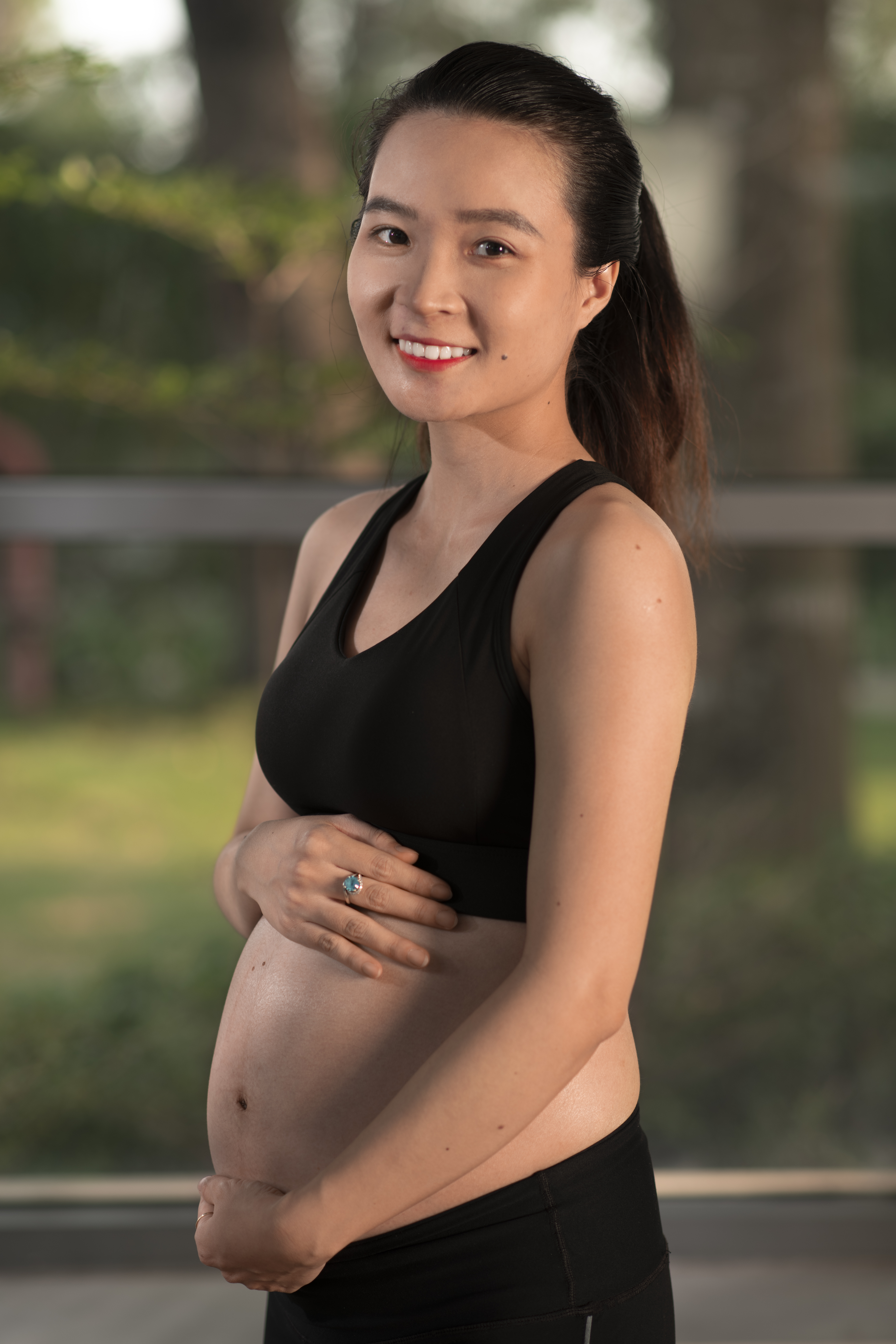 smiling pregnant woman in athletic wear holding her belly after visiting a fertility clinic in cupertino ca.