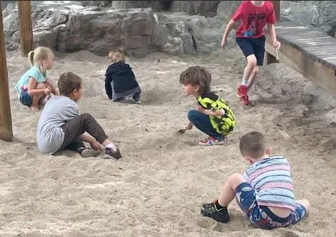 Child writes A in green sand