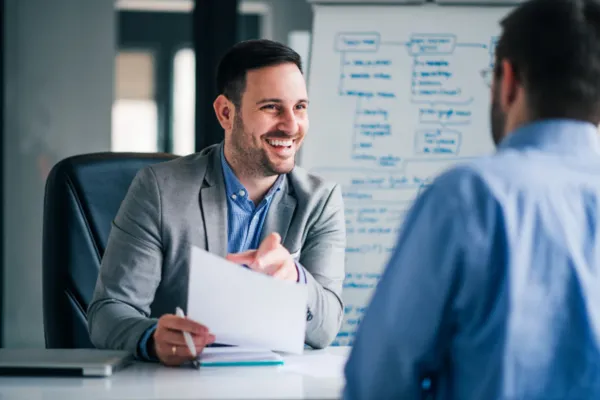 In an office, one man speaks to another, illustrating a dialogue in a business context.