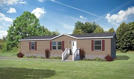 A single-story manufactured home with brown siding, white trim, and a front porch, set in a grassy area surrounded by trees under a clear blue sky; this Houston Apex property offers serene living at its finest.