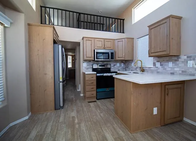 Modern kitchen with wooden cabinets, stainless steel appliances including a microwave and oven, quartz countertops, tiled backsplash, and a high ceiling with upper loft railings—a stunning example of J Houston Properties' commitment to quality.