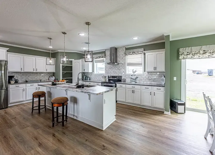 Modern kitchen with white cabinets, stainless steel appliances, a central island with seating, and green walls. The room features wooden flooring and large windows providing natural light.