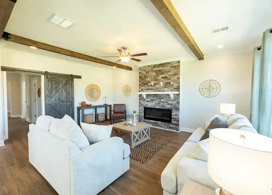 A modern, open-concept living space featuring a kitchen with an island, a dining area, and a living room with a sofa and wall-mounted TV. The decor includes framed art and various household items.