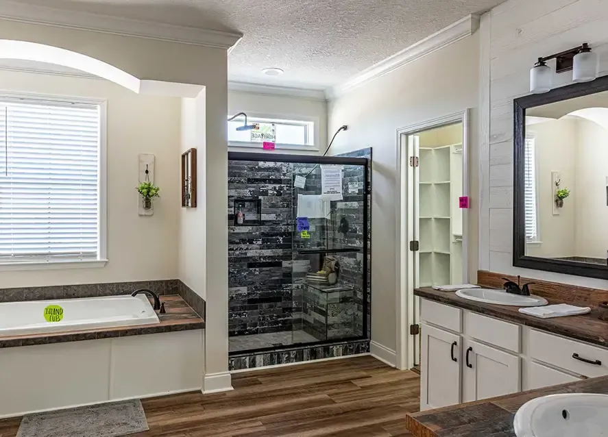 A modern, open-cModern bathroom with a bathtub, glass-enclosed shower, sink with a mirror, and a walk-in closet. The floor is wooden, and the walls are light-colored.oncept living space featuring a kitchen with an island, a dining area, and a living room with a sofa and wall-mounted TV. The decor includes framed art and various household items.