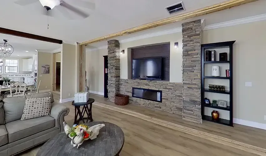 A living room at Houston Woodland Properties features a stone accent wall with a mounted TV and fireplace, flanked by a bookshelf and couch. The dining area is visible in the background, completing the inviting ambiance.