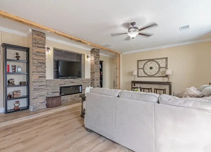 A modern kitchen with wooden cabinets, black appliances, and granite countertops. A vase with red tulips is on the counter. The living area has a sofa, round coffee table, and a rug.