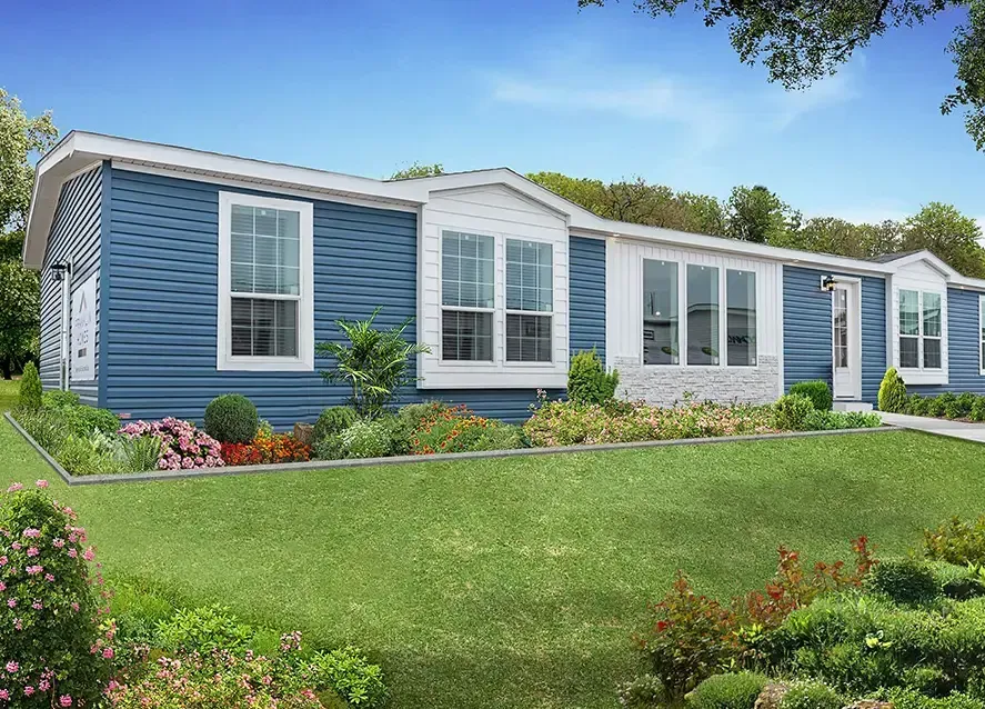 A light blue manufactured home with white trim sits amid a well-maintained green lawn and colorful flower beds, under a clear Houston sky.