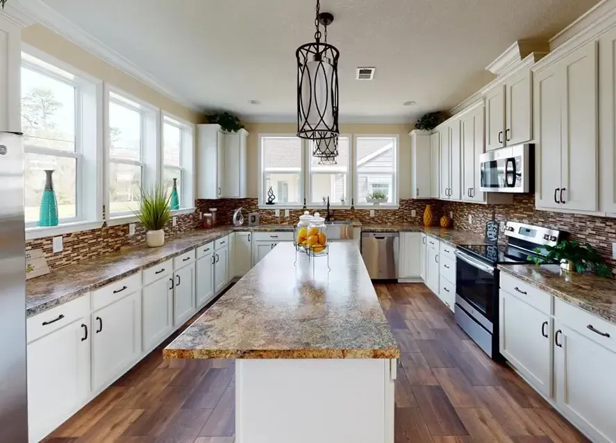 Spacious kitchen with white cabinets, a large granite island, stainless steel appliances, wooden floors, and several windows providing natural light in this Houston Lilly II manufactured home.