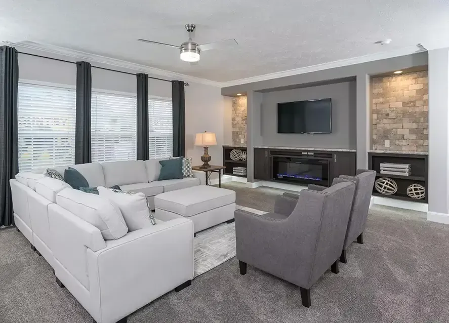 A modern living room setup in a Houston modular home features a wall-mounted TV above a fireplace. Shelves on either side contain decorative items and folded blankets, while the walls boast a stone-textured finish, epitomizing the charm you'd expect from a Somerset design.