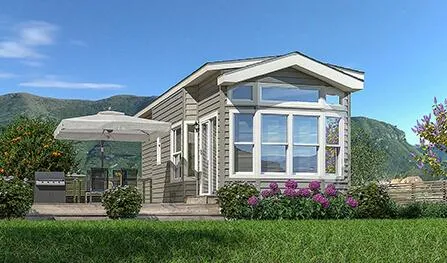 A small, single-story house with large windows and a patio featuring outdoor furniture, an umbrella, shrubs, and purple flowers in a garden setting with hills in the background evokes the charm of Malibu Park Model Homes.